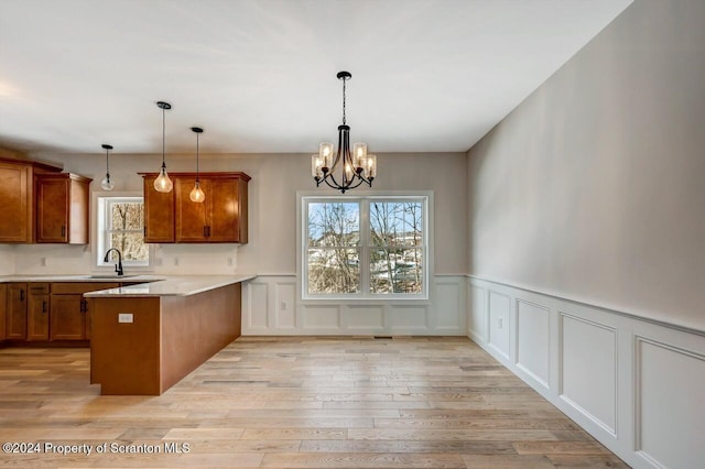 kitchen with a peninsula, a sink, light wood-style flooring, and brown cabinets