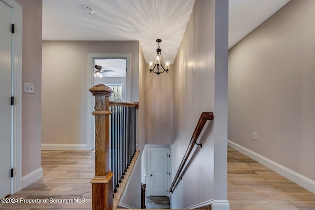 stairway with an inviting chandelier, wood finished floors, and baseboards