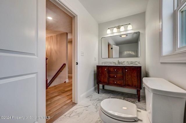 half bathroom with toilet, marble finish floor, baseboards, and vanity