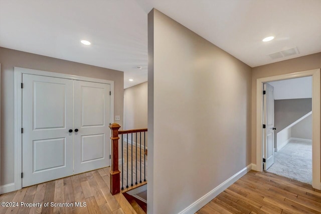 corridor with light wood-style flooring, an upstairs landing, visible vents, and baseboards