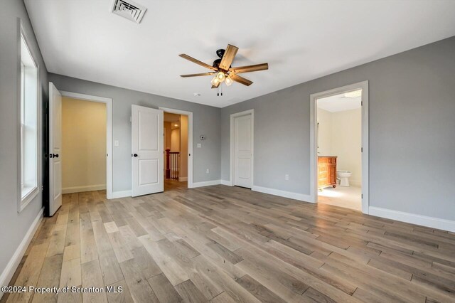 unfurnished bedroom featuring ceiling fan, a closet, light hardwood / wood-style flooring, and ensuite bath