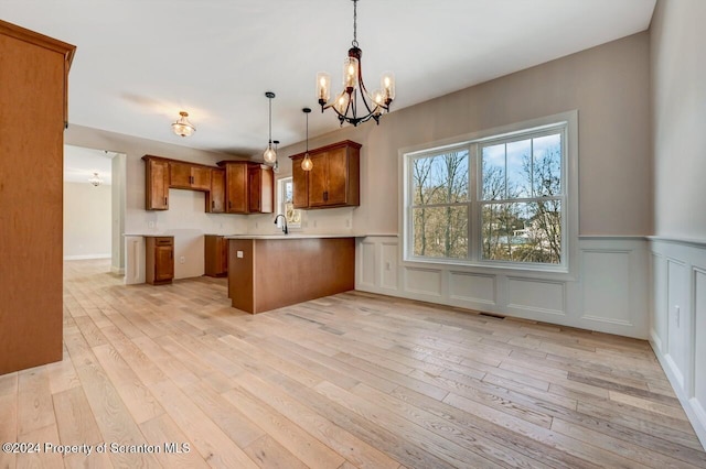 kitchen with light wood finished floors, brown cabinetry, a peninsula, an inviting chandelier, and pendant lighting