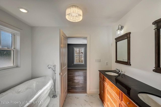 full bath with marble finish floor, double vanity, a sink, a freestanding tub, and baseboards