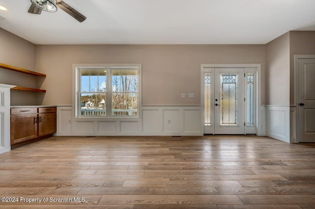 entrance foyer with light wood finished floors, a ceiling fan, and wainscoting