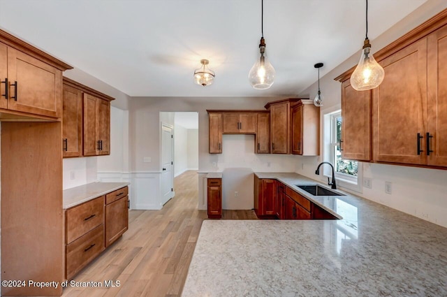 kitchen with light stone counters, sink, pendant lighting, and light hardwood / wood-style floors