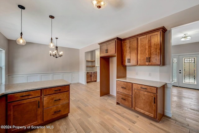 kitchen with a wainscoted wall, brown cabinetry, light wood-type flooring, and decorative light fixtures