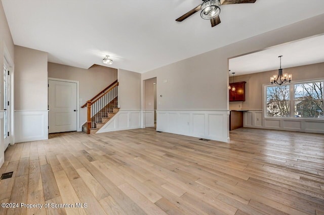 unfurnished living room featuring ceiling fan with notable chandelier and light wood-type flooring