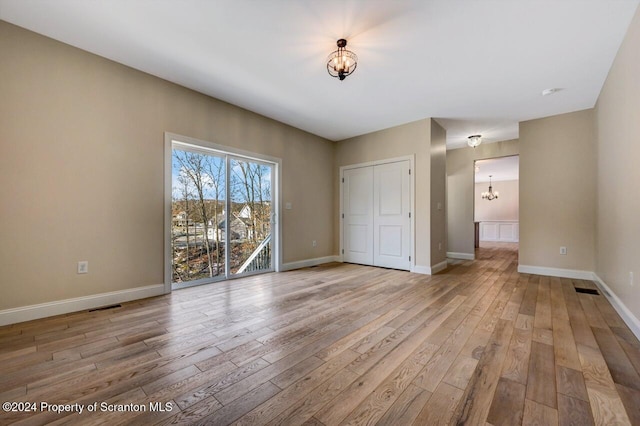 unfurnished bedroom with a notable chandelier, light wood-style flooring, visible vents, and baseboards