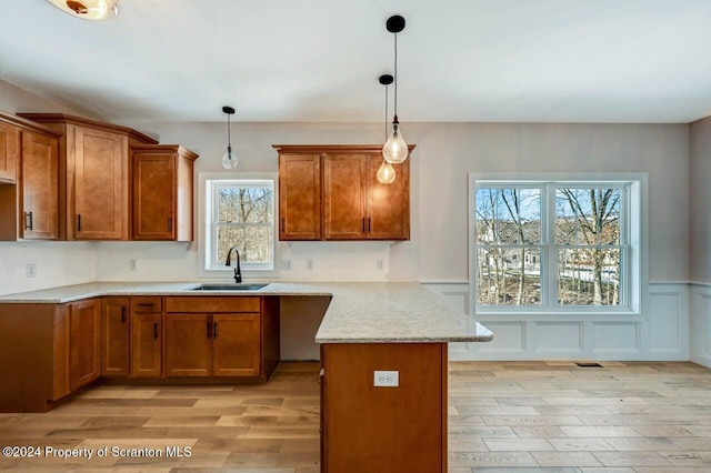 kitchen featuring a peninsula, light wood finished floors, brown cabinetry, and a sink