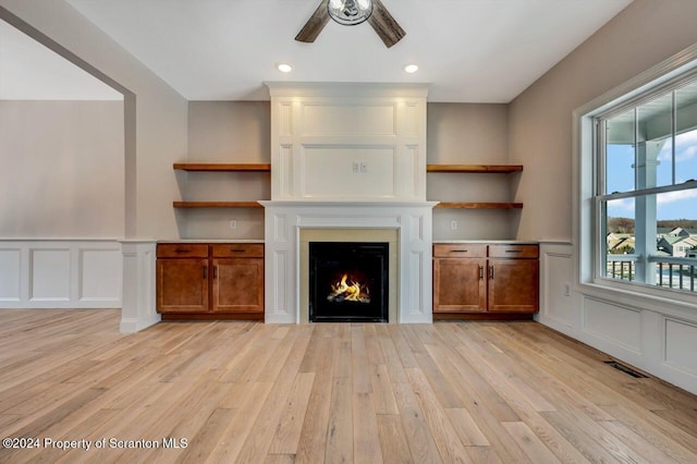 unfurnished living room featuring ceiling fan, light wood-style flooring, a fireplace, and a decorative wall