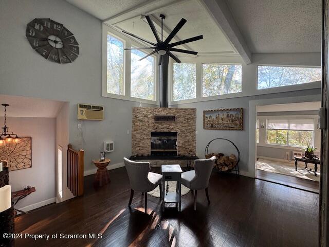 dining room with beam ceiling, ceiling fan, dark wood-type flooring, a stone fireplace, and an AC wall unit