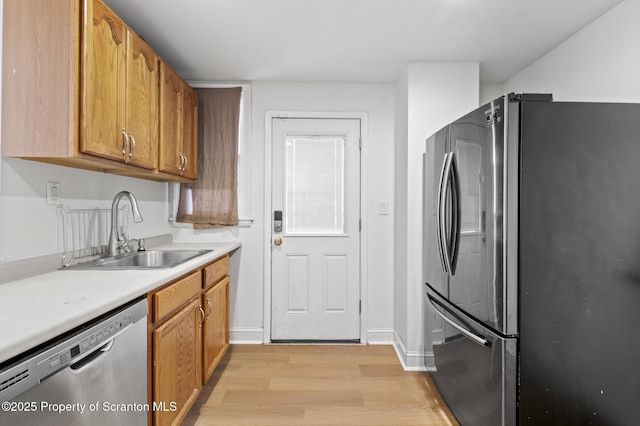 kitchen featuring appliances with stainless steel finishes, a sink, light countertops, brown cabinetry, and light wood-style flooring