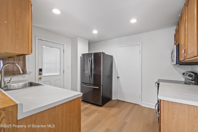 kitchen with a sink, appliances with stainless steel finishes, light wood-type flooring, and light countertops