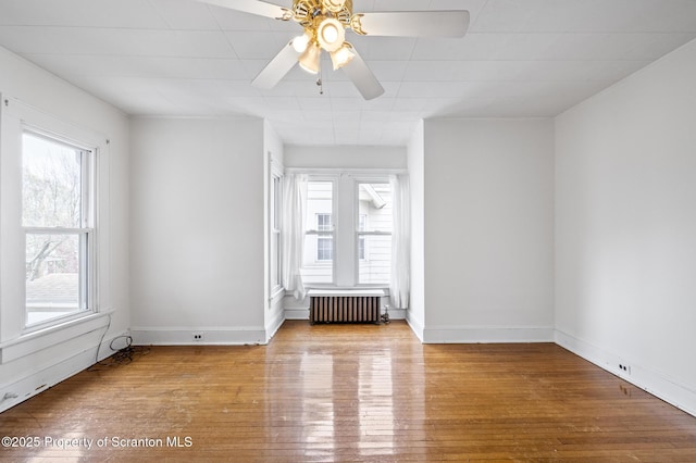 unfurnished room featuring a ceiling fan, baseboards, radiator heating unit, and wood finished floors