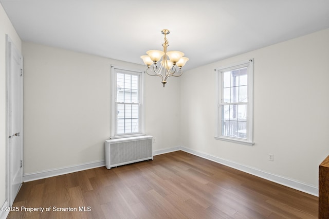 spare room featuring an inviting chandelier, baseboards, radiator heating unit, and wood finished floors