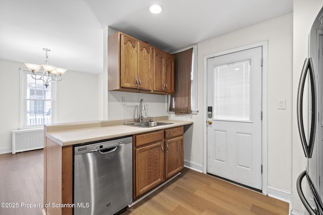 kitchen with brown cabinets, a sink, radiator heating unit, light wood-style flooring, and stainless steel appliances