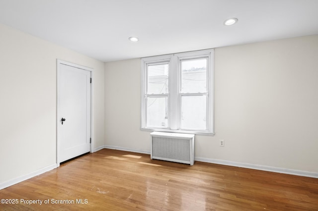 empty room with radiator heating unit, baseboards, recessed lighting, and light wood-type flooring