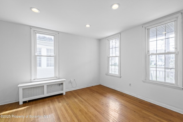 spare room featuring recessed lighting, baseboards, radiator, and light wood-style floors