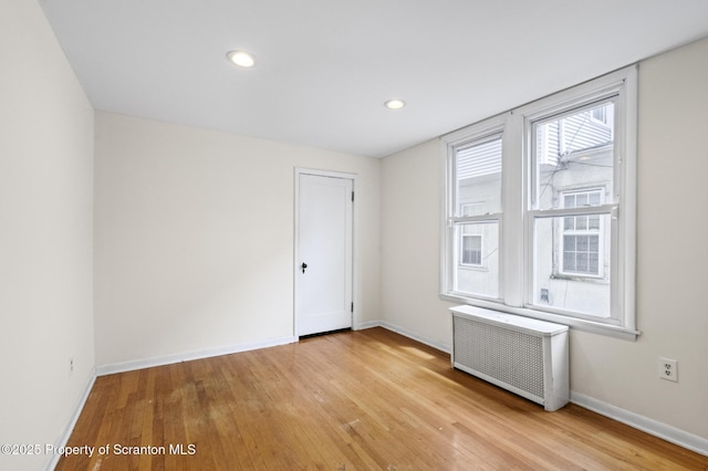 unfurnished room with recessed lighting, radiator, baseboards, and light wood-type flooring