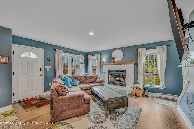 living room featuring light hardwood / wood-style floors, a stone fireplace, and a baseboard heating unit