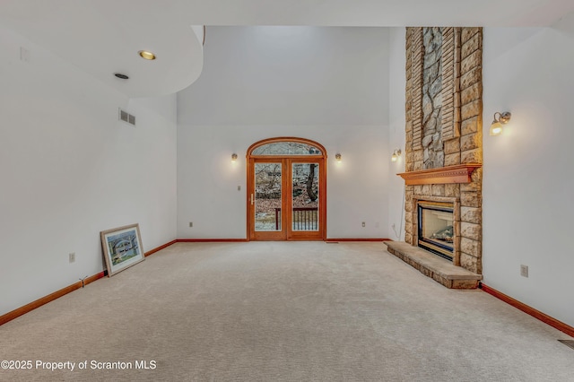 unfurnished living room featuring a towering ceiling, visible vents, carpet flooring, and a stone fireplace