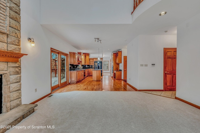 kitchen with light carpet, a high ceiling, black refrigerator with ice dispenser, a fireplace, and pendant lighting