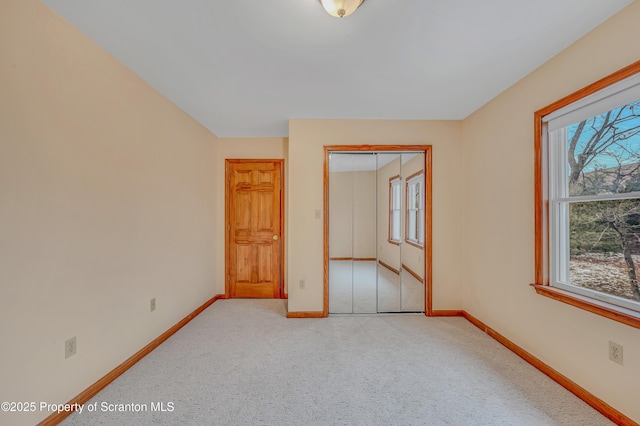 unfurnished bedroom with a closet, light colored carpet, and baseboards