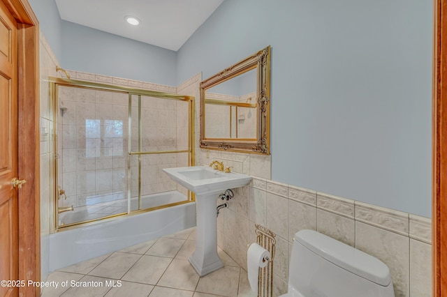 full bathroom featuring wainscoting, toilet, tile patterned floors, combined bath / shower with glass door, and tile walls