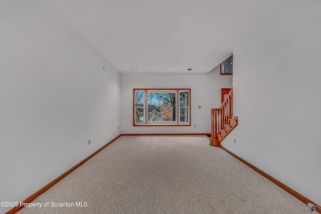 unfurnished living room featuring baseboards, stairway, and carpet flooring