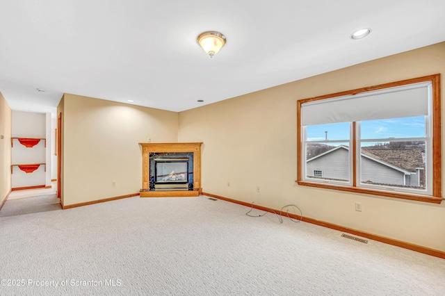 unfurnished living room with carpet floors, baseboards, visible vents, and a glass covered fireplace