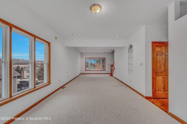 empty room featuring a healthy amount of sunlight, baseboards, built in features, and light colored carpet