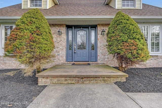entrance to property featuring a shingled roof and brick siding