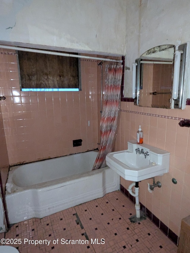 bathroom with tiled shower / bath combo, sink, and tile walls