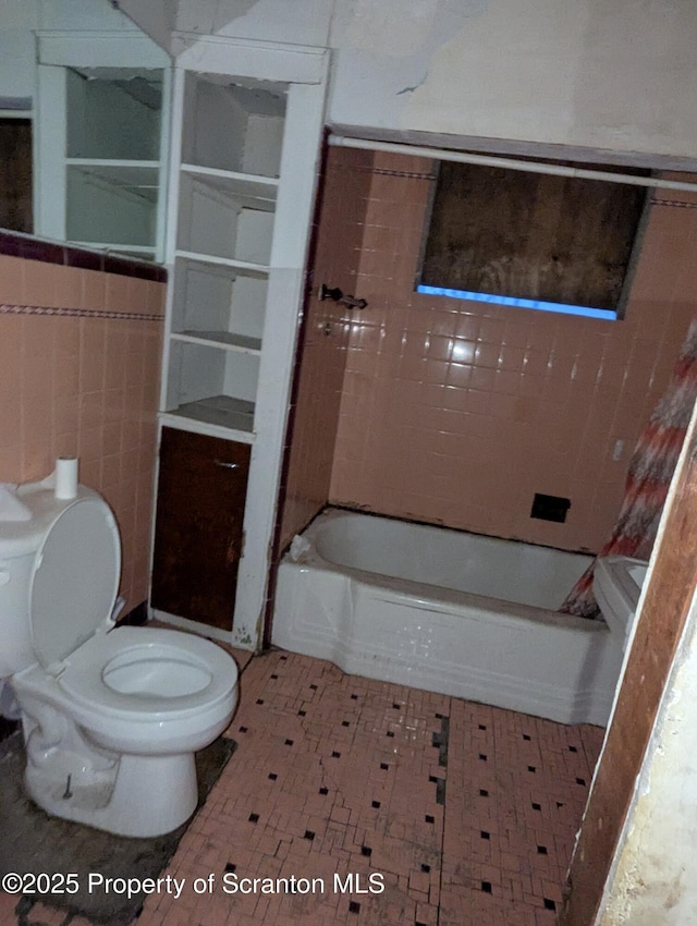 bathroom featuring tile walls, a bath, and toilet