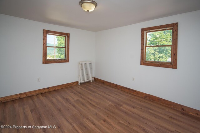 empty room with a healthy amount of sunlight, radiator heating unit, and dark wood-type flooring