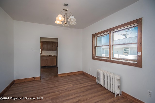 empty room with dark hardwood / wood-style flooring, an inviting chandelier, and radiator