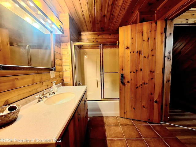 bathroom with wooden ceiling, tile patterned floors, shower / bath combination with glass door, wooden walls, and vanity