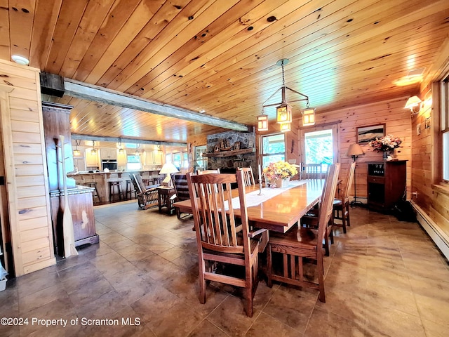 dining room with a stone fireplace, wooden ceiling, wooden walls, and a baseboard radiator