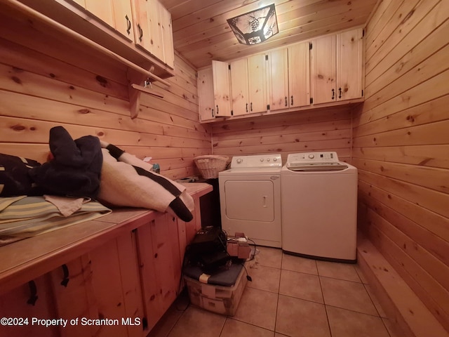 clothes washing area with separate washer and dryer, wood walls, light tile patterned flooring, and cabinets