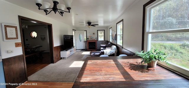 living room featuring a fireplace, ceiling fan with notable chandelier, wooden walls, and a healthy amount of sunlight