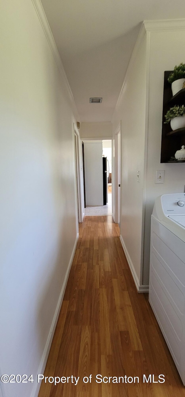 corridor with washer / clothes dryer, crown molding, and wood-type flooring