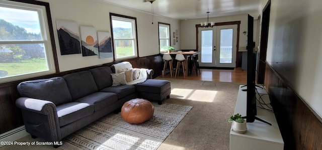 carpeted living room featuring wooden walls, french doors, a baseboard heating unit, and a notable chandelier