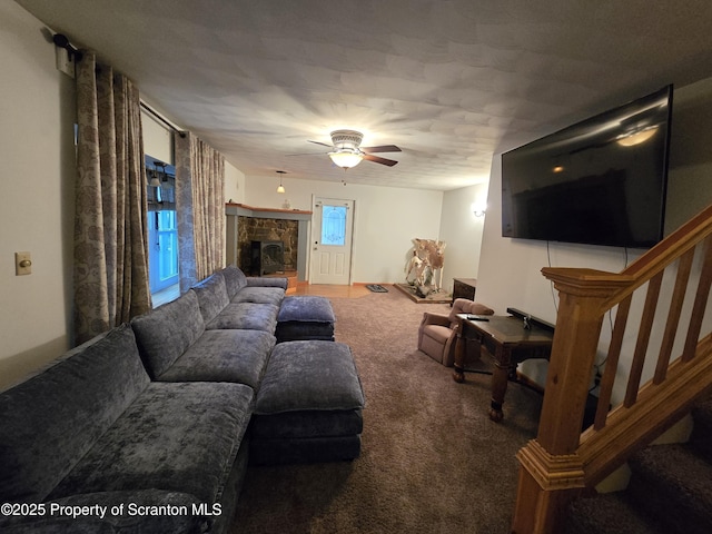 carpeted living room with ceiling fan and a stone fireplace