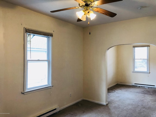 unfurnished room featuring plenty of natural light, baseboard heating, arched walkways, and dark colored carpet