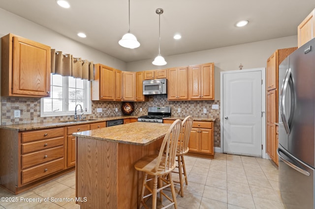 kitchen featuring appliances with stainless steel finishes, hanging light fixtures, light stone counters, a kitchen island, and sink