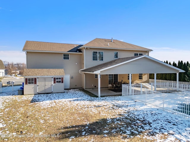 snow covered rear of property featuring a storage shed and a patio