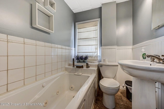 bathroom with toilet, a tub with jets, and wainscoting