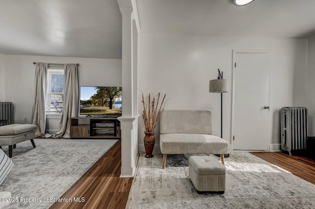 sitting room featuring radiator, decorative columns, and wood finished floors