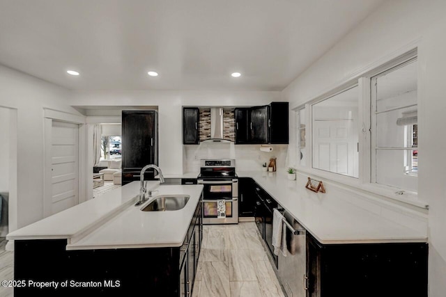 kitchen with range with two ovens, dark cabinets, a sink, light countertops, and wall chimney exhaust hood