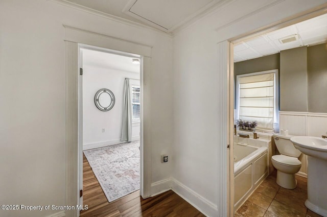 bathroom featuring a garden tub, visible vents, ornamental molding, wainscoting, and wood finished floors